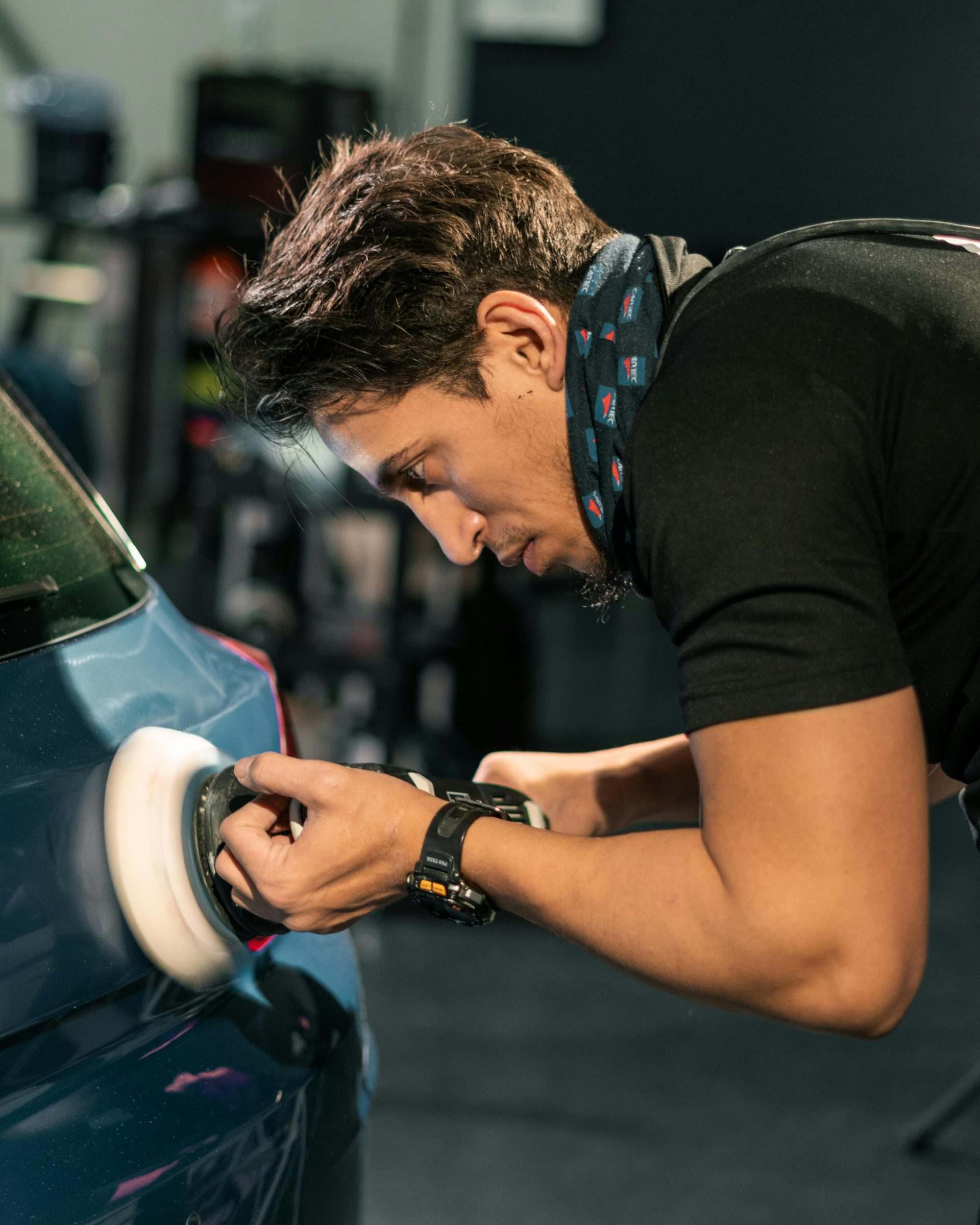 A man polishing a car with a buffing machine in an indoor setting.